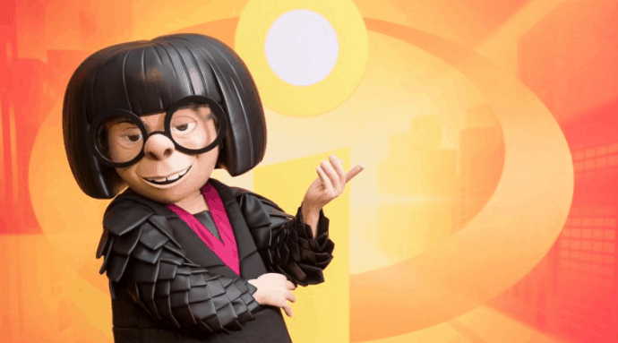 Edna Mode strikes a pose before the glowing Incredibles logo backdrop at Walt Disney World.
