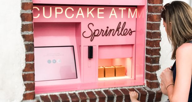 Enjoying Disney Springs, guests grab fresh treats from the pink Sprinkles cupcake ATM built into a brick wall—so convenient!.