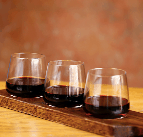 Trio of red wines on a wooden tray at Maria & Enzo's in Disney Springs, set on a rustic table—cheers to National Wine Day!.