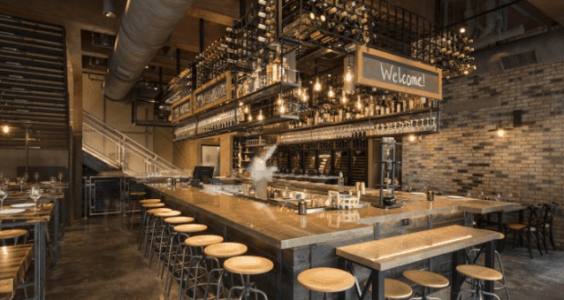 Trendy bar with wooden stools, hanging lights, and a "Welcome!" sign—evoking the vibe of Wine Bar George at Disney Springs.