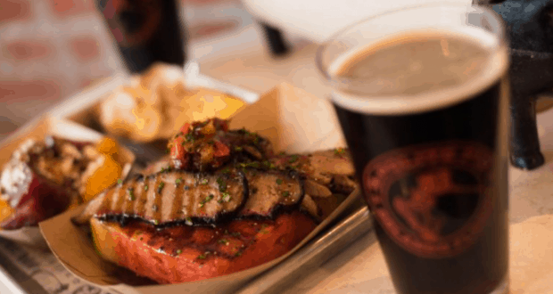 A festive platter of smoky BBQ meats and sides, paired with a frothy brew—perfect for refueling between theme park thrills.