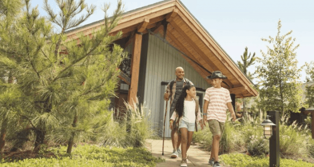 Guests stroll along a lush garden path by a cozy wooden cabin at Disney Vacation Club Resort in Walt Disney World.