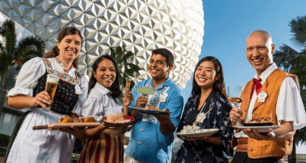 Guests dressed in playful festival outfits enjoy drinks and gourmet bites outside Epcot’s iconic geodesic dome at Food & Wine.