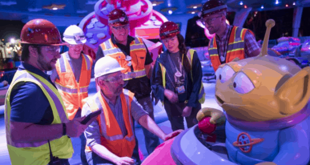 Cast Members in safety vests and helmets inspect a giant Toy Story alien figure, capturing the whimsical spirit of Toy Story Land.