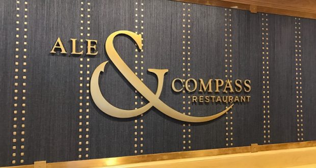 The gold "Ale & Compass Restaurant" sign gleams on a blue wall, inviting Disney World guests into this chic dining haven.