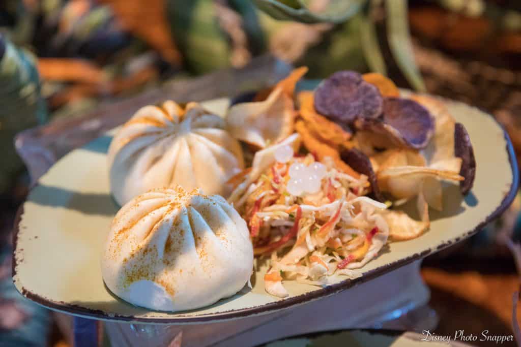 Steamed buns, slaw with popping pearls, and veggie chips on a pastel green plate—Disney World quick-service at its best.