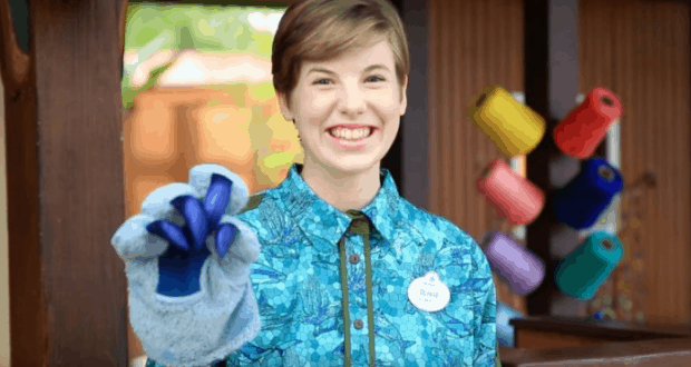 A Cast Member in blue brings the magic backstage, showing off a Blue's Clues paw puppet amid colorful spool props.