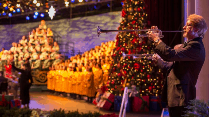 A trumpet player performs by a Christmas tree as the gold-robed choir sings during Epcot’s Candlelight Processional.