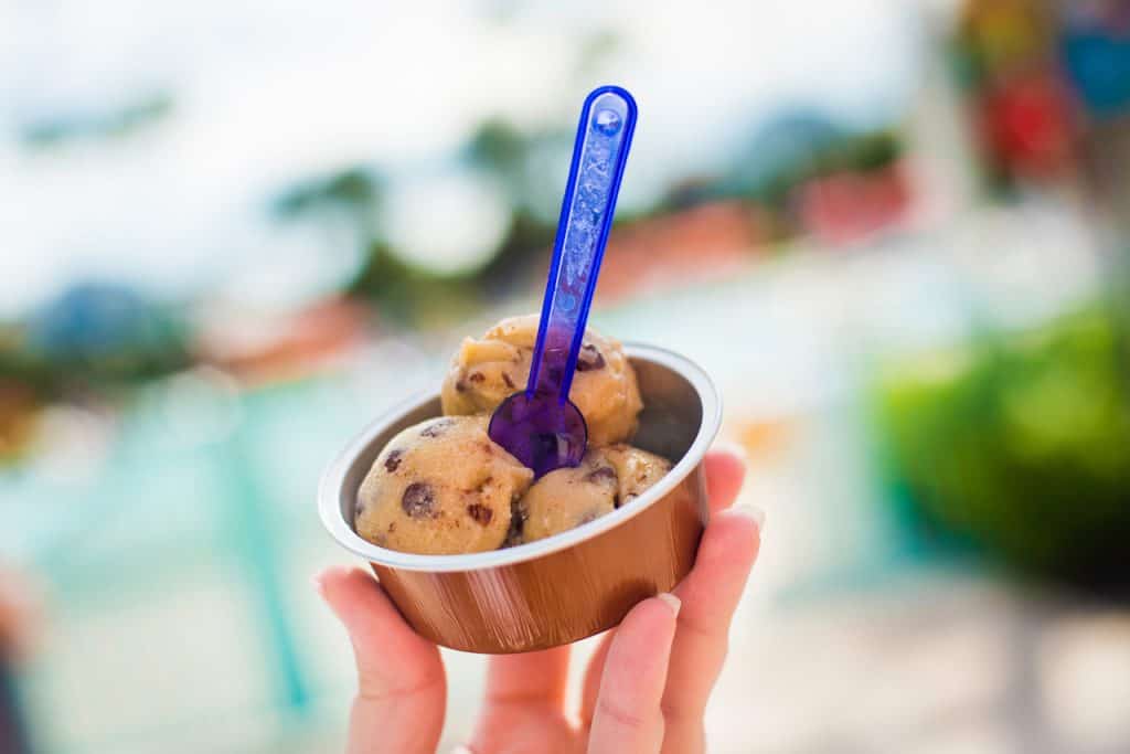 A guest enjoys classic Disney cookie dough in a small cup, scooped with a blue spoon—just one of many must-try park treats.