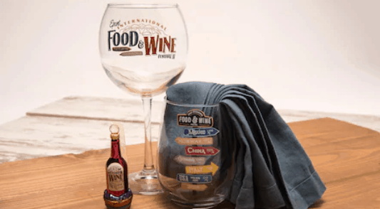 Epcot Food & Wine Festival wine glass, napkin-lined glass, and festival bottle magnet displayed on a wooden table.