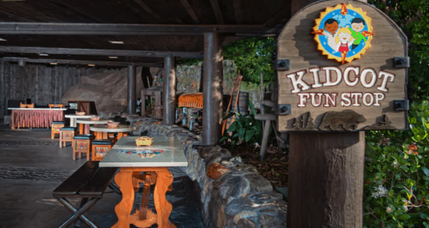 Kidcot Fun Stops sign and wooden-sheltered seating surrounded by lush greenery, a relaxing retreat in Epcot’s World Showcase.
