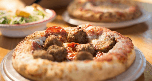Pepperoni and meatball pizza, with salad and another pie behind, highlights fresh dining options at Disney World restaurants.