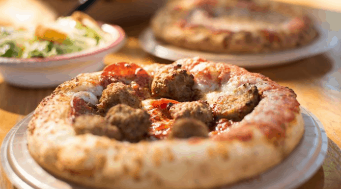 Pepperoni and meatball pizza, with salad and another pie behind, highlights fresh dining options at Disney World restaurants.