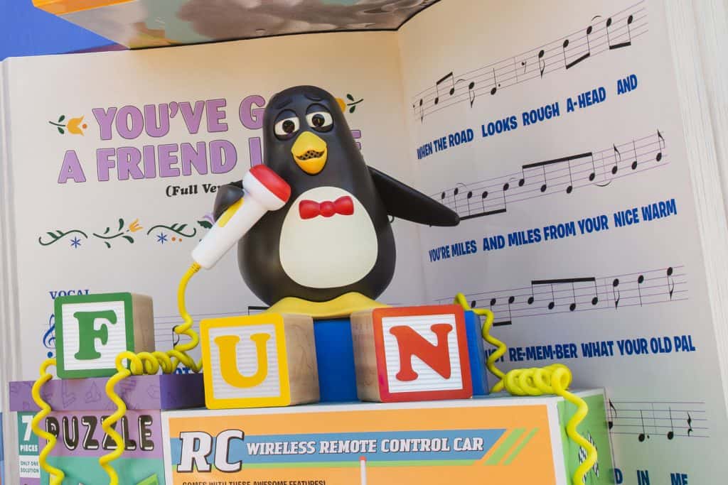 Wheezy the penguin belts a tune on letter blocks before "You've Got a Friend" sheet music, channeling Slinky Dog Dash vibes.