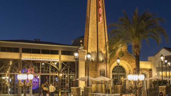 Guests stroll past The Edison at Disney Springs, its iconic neon sign glowing against the vibrant night entertainment scene.