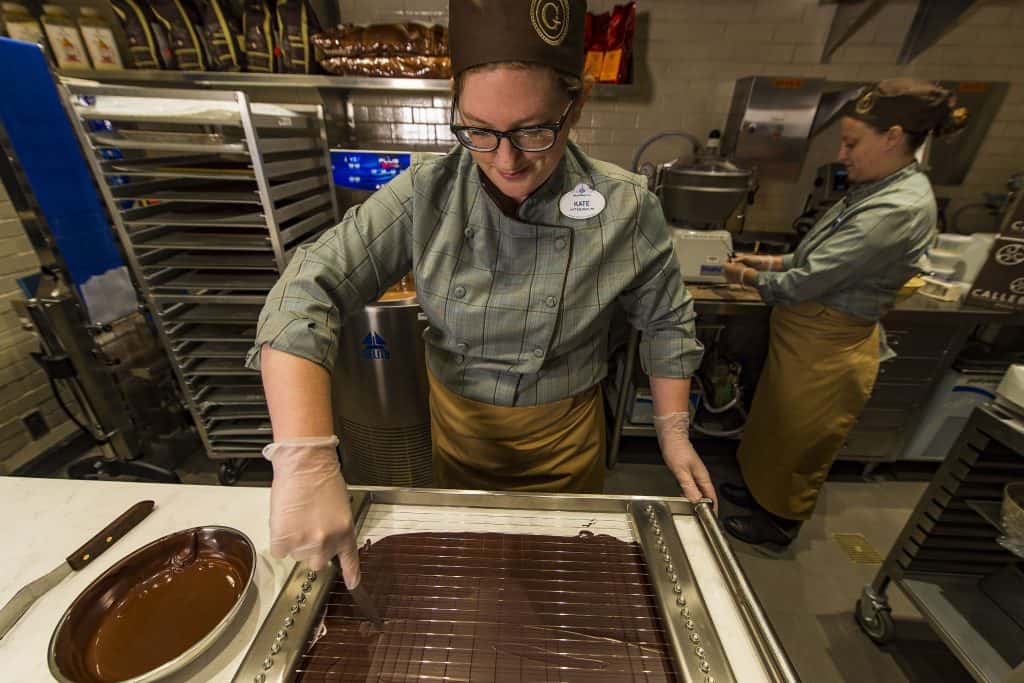 A Disney Springs chocolatier in uniform slices fresh chocolate, with another team member nearby—a must-stop for Walt Disney World fans.