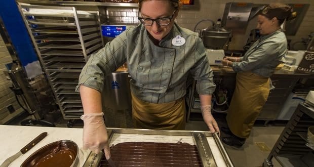 A Disney Springs chocolatier in uniform slices fresh chocolate, with another team member nearby—a must-stop for Walt Disney World fans.