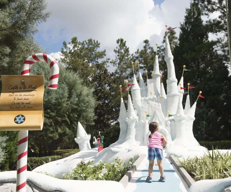 A young guest gazes at a whimsical white Disney castle, lush greenery around, and a candy cane sign welcoming families to magical fun.