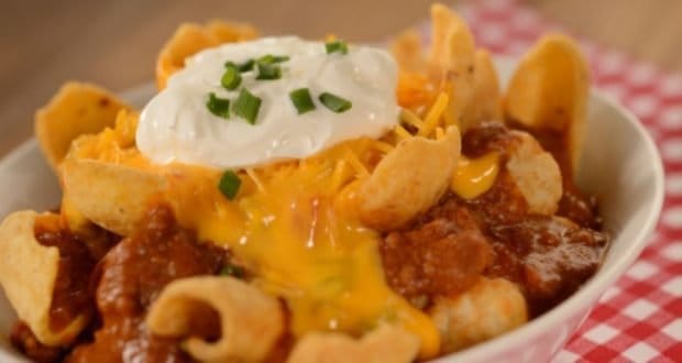 Chili topped with corn chips, cheese, sour cream, and green onions on a red checkered cloth at Woody’s Lunch Box in Disney World.
