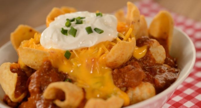 Chili topped with corn chips, cheese, sour cream, and green onions on a red checkered cloth at Woody’s Lunch Box in Disney World.
