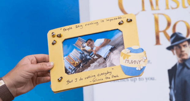 A guest showcases a cheerful Winnie the Pooh photo frame, featuring a beach scene and playful honey pot accent at Disneyland.
