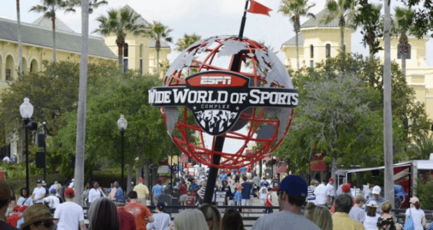 Guests bustle around the ESPN Wide World of Sports globe at Disney, amid palms, lively buildings, and Labor Day Fan Zone excitement.