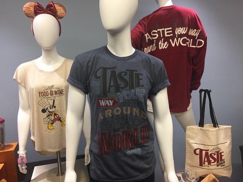 Epcot Food & Wine Festival shirts on display with a 2018 “Taste” tote bag, perfect for Disney fans and park goers.