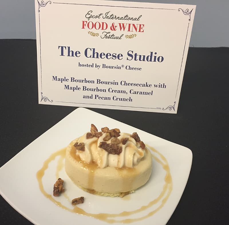 Decadent cheesecake with cream, caramel, and pecans at the 2018 Epcot Food & Wine Festival, Disney World, sign in back.