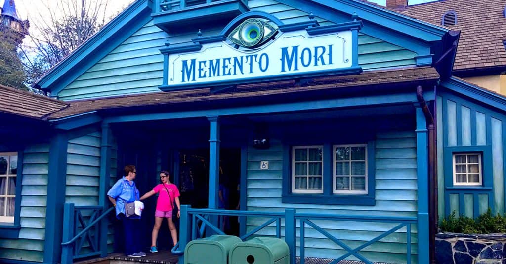 Memento Mori gift shop at Magic Kingdom, iconic blue exterior, fans chatting outside, classic Disney trash can nearby.