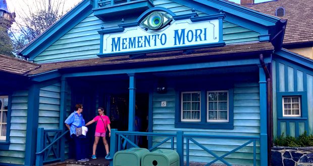 Memento Mori gift shop at Magic Kingdom, iconic blue exterior, fans chatting outside, classic Disney trash can nearby.