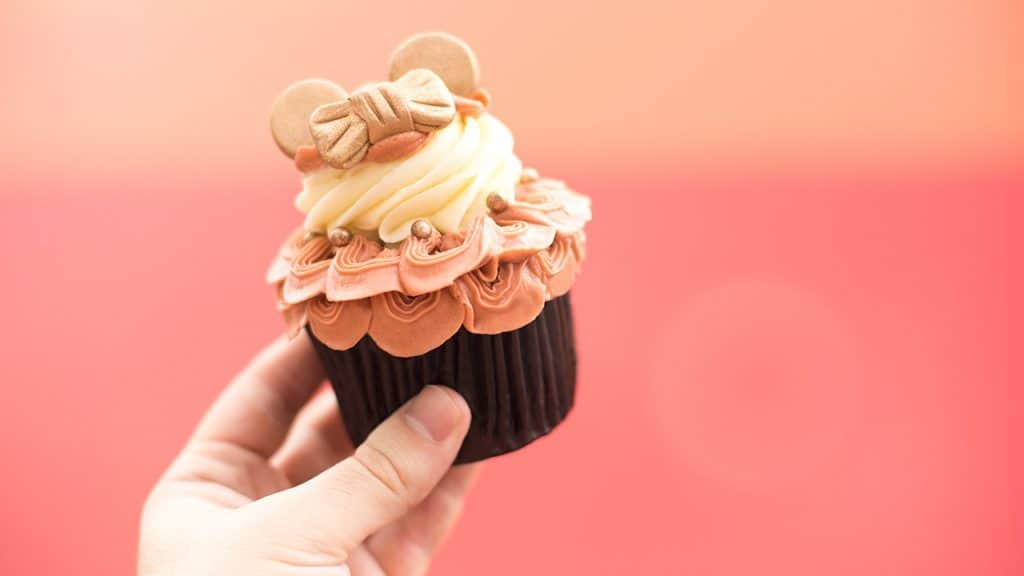 Indulge in a Disney World cupcake topped with pink and white frosting and a Minnie Mouse-shaped cookie—pure park magic!.