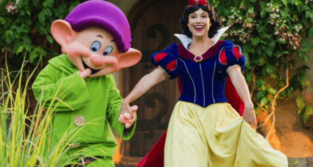Snow White and Dopey share a joyful moment hand in hand in the lush gardens at Storybook Dining, Disney’s Artist Point.