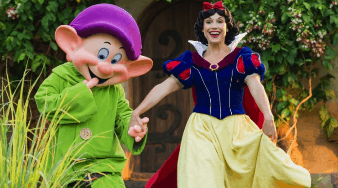 Snow White and Dopey share a joyful moment hand in hand in the lush gardens at Storybook Dining, Disney’s Artist Point.