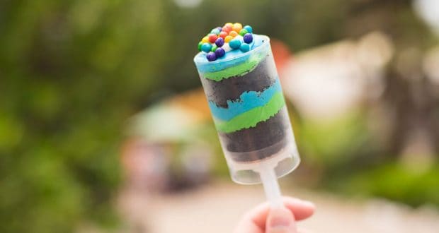 Hand holding a colorful push pop dessert topped with candy, set against lush greenery—just like treats at Disney’s Animal Kingdom.