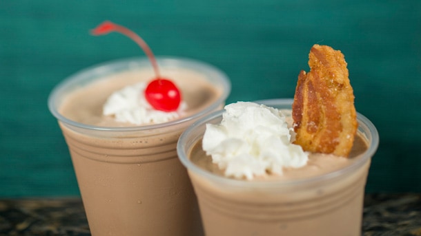 Sip Animal Kingdom-inspired chocolate milkshakes in plastic cups—one crowned with a cherry, the other bacon—for a park-worthy treat!.