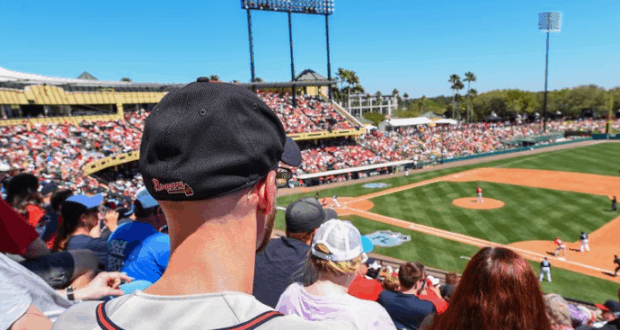 Fans enjoy Atlanta Braves Spring Training under the sun, viewed from behind a guest in a black cap at the ballpark.