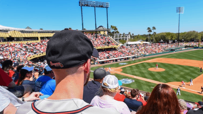 Fans enjoy Atlanta Braves Spring Training under the sun, viewed from behind a guest in a black cap at the ballpark.
