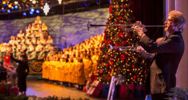 A trumpeter performs onstage at Disney World’s Candlelight Processional, framed by a sparkling Christmas tree and golden-robed choir.