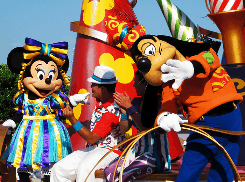 Minnie Mouse, Goofy, and a lively performer show off vibrant dance moves at Disney World’s energetic Move It Shake It parade.