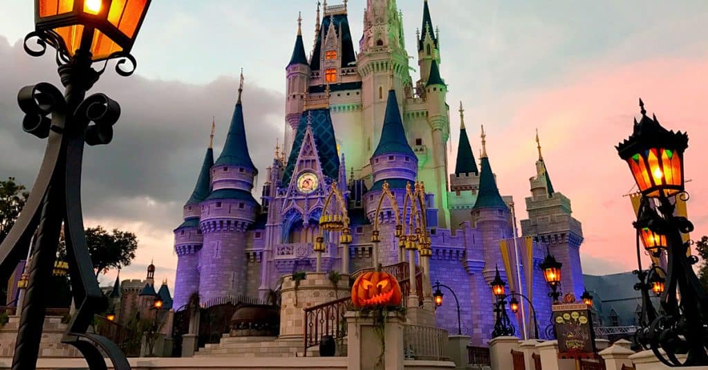 Cinderella Castle glowing with vibrant lights at sunset, featuring a giant jack-o'-lantern for Disney World's Halloween celebration.