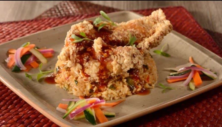 Savor crispy fried chicken over rice with sauce and fresh veggies, served on a square plate at Walt Disney World’s top spots.