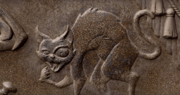 Stone carving of a fierce, hissing cat with arched back and bared teeth, setting a spooky mood for the Haunted Mansion queue.