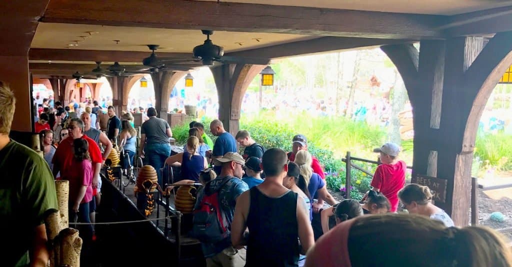 Guests line up under shaded queues at Disney World, with sunlight streaming in and lush greenery setting the magical scene.