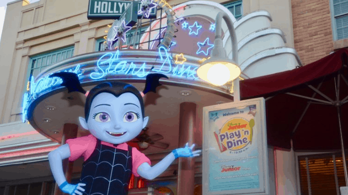 Vampirina greets guests outside the neon Play 'n Dine at Disney’s Hollywood Studios, glowing with playful Disney energy.