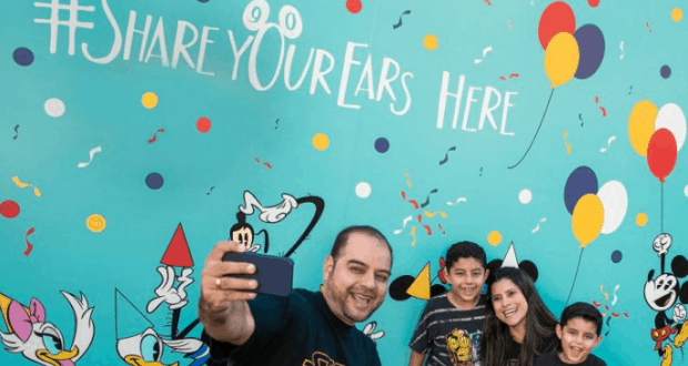 Guests snap a selfie at the vibrant Disney Ear Wall in Walt Disney World, surrounded by colorful balloons and beloved characters.
