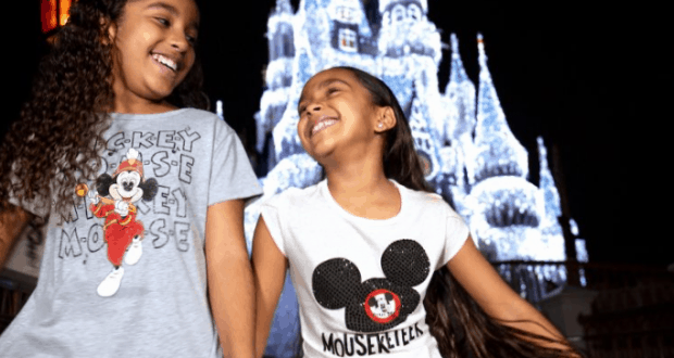 Two girls in Mickey Mouse shirts pose by a glowing Cinderella Castle at night, celebrating the magic of Disney World together.