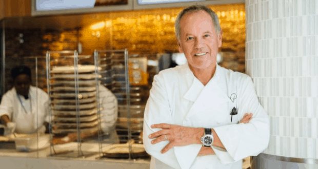 Wolfgang Puck beams in his chef whites at the new Bar & Grill, as staff bustle behind him at Walt Disney World.