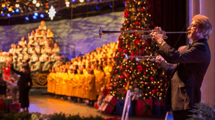 A trumpeter performs onstage with a massive choir and sparkling Christmas tree at Walt Disney World’s magical Candlelight Processional.