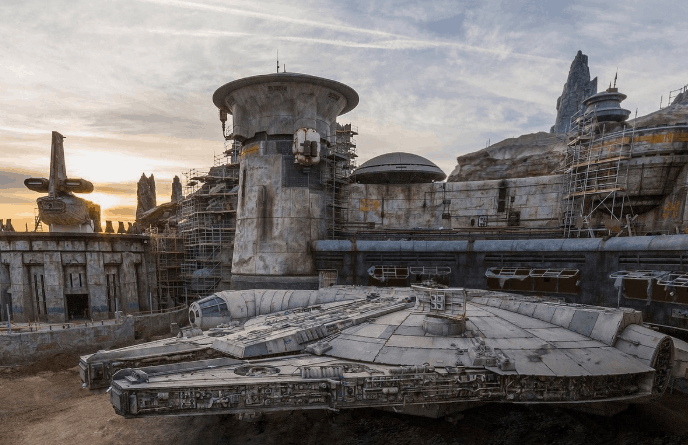 The Millennium Falcon docked at Star Wars: Galaxy’s Edge, surrounded by Batuu’s sci-fi architecture at sunset in Disney World.