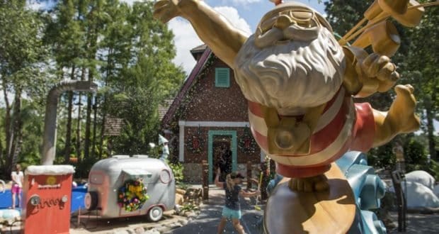 Santa Claus in swim trunks greets guests by a festive house and trailer, with snowy fun at Winter Summerland Miniature Golf.